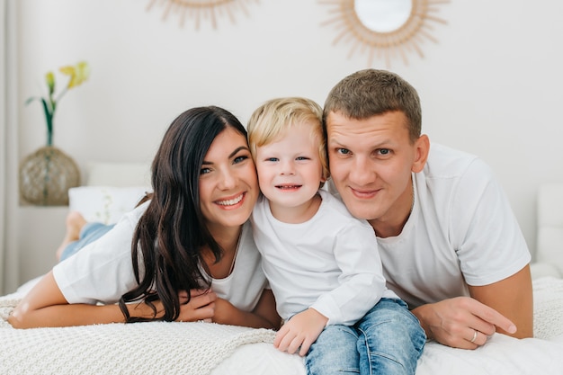 Retrato de uma família caucasiano feliz, deitada na cama e batendo enquanto olha para a câmera no quarto em casa.