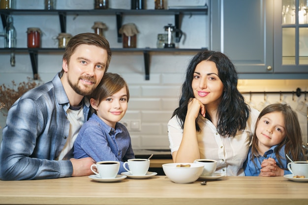 Foto retrato de uma família feliz, bebendo chá com biscoitos na cozinha.