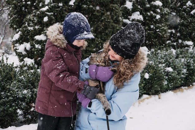 Retrato de uma família feliz, mãe, filho e gato no parque de inverno nevado, retrato ao ar livre de mãe e filho