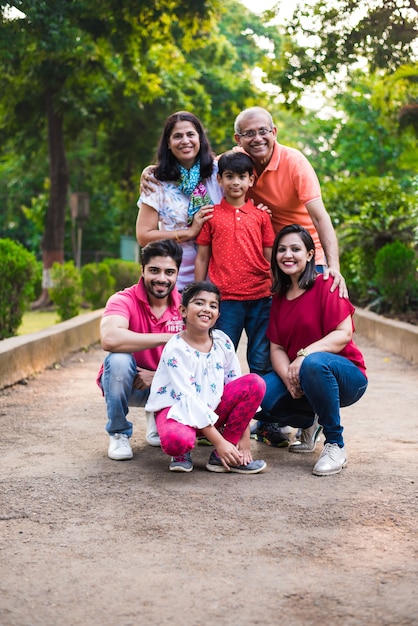 Retrato de uma família indiana de seis, desfrutando de um piquenique ou caminhada matinal - várias gerações de família asiática, posando em uma passarela no parque, ao ar livre. foco seletivo