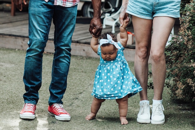 Retrato de uma família inter-racial sincera e feliz caminhando com um bebê moreno de mãos dadas no parque de campismo