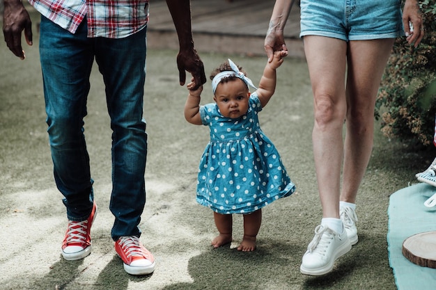 Retrato de uma família inter-racial sincera e feliz caminhando com um bebê moreno de mãos dadas no parque de campismo