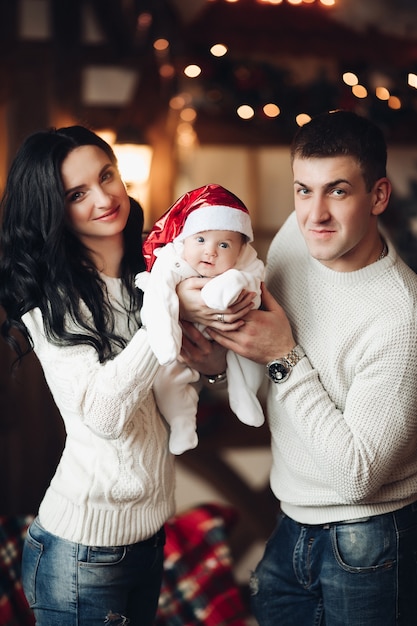 Retrato de uma família jovem e adorável segurando seu filho bebê com chapéu de Papai Noel vermelho