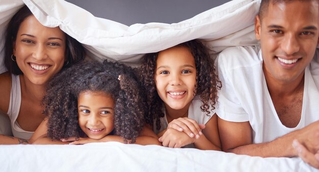 Foto retrato de uma família negra feliz se unindo em uma cama relaxe e sorria em um quarto juntos cobertor de amor e pais felizes aproveitando o tempo livre com seus filhos sendo brincalhões e apaixonados pela manhã