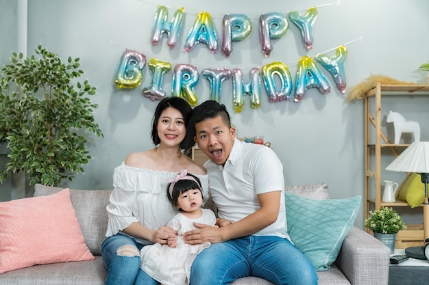 retrato de uma família nuclear asiática feliz olhando para a câmera durante a festa de aniversário em uma sala decorada em casa