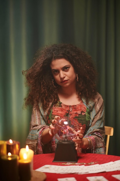 Retrato de uma feiticeira séria usando uma bola de cristal para ver a fortuna do cliente