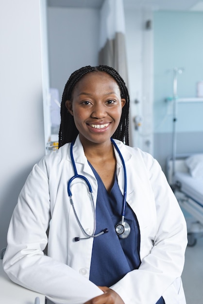 Retrato de uma feliz médica afro-americana vestindo uma bata de laboratório e um estetoscópio em um quarto de hospital