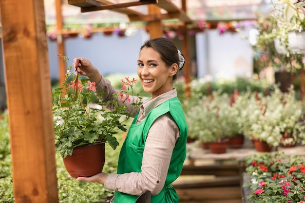 Retrato de uma florista linda jovem segurando o vaso de flores em um centro de jardim.