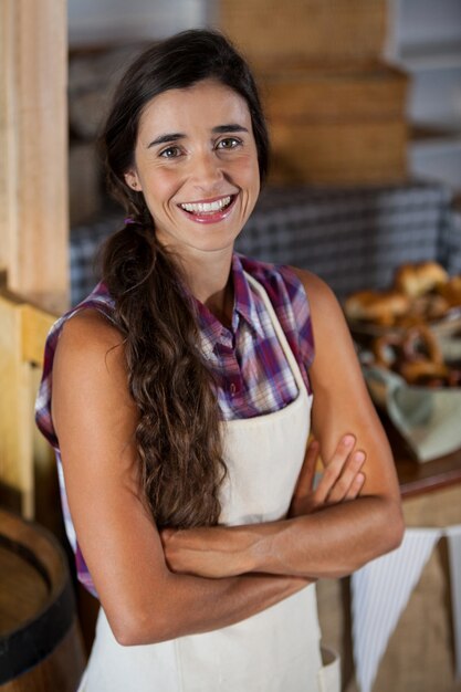 Foto retrato de uma funcionária sorridente em pé com os braços cruzados na padaria