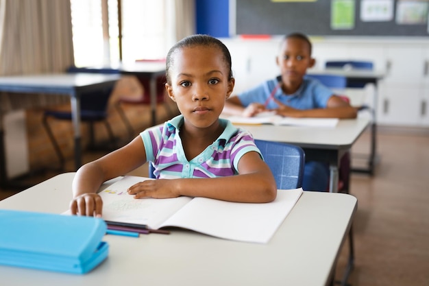 Retrato de uma garota afro-americana sentada em sua mesa na classe na escola