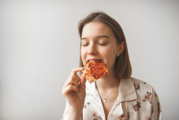 Retrato de uma garota atraente comendo um pedaço de pizza com os olhos fechados