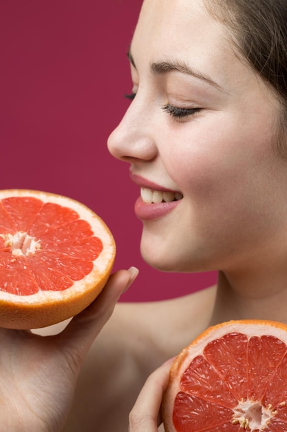 Retrato de uma garota atraente segurando uma fatia de toranja em um fundo vermelho