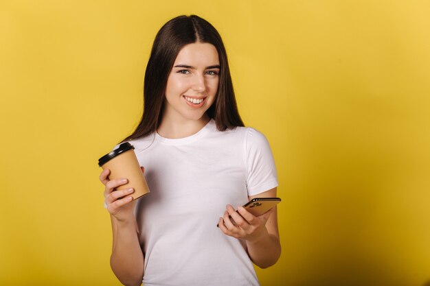 Retrato de uma garota atraente usando o telefone e segurando uma xícara de café