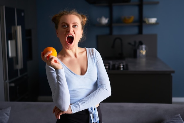 Retrato de uma garota bonita caucasiana fazendo caretas segurando laranja fresca e suculenta em casa em