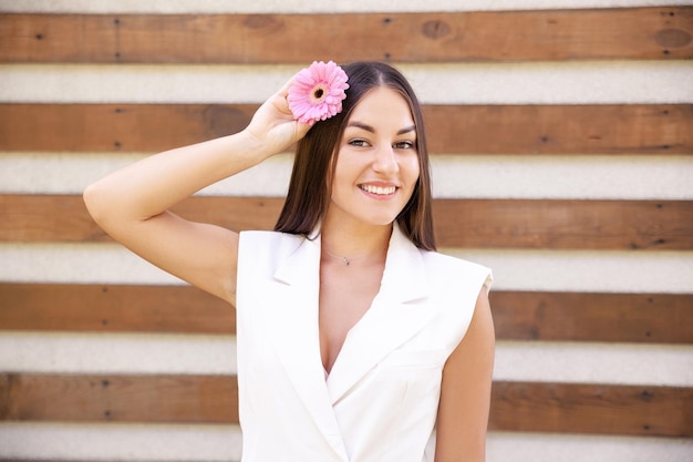 Retrato de uma garota caucasiana feliz em roupas brancas com uma flor rosa no cabelo