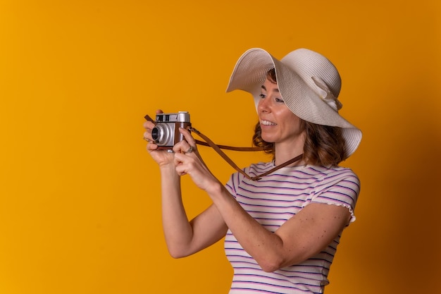 Retrato de uma garota caucasiana no conceito de turista sorrindo com um chapéu e óculos de sol tirando uma foto e aproveitando o fundo amarelo das férias de verão