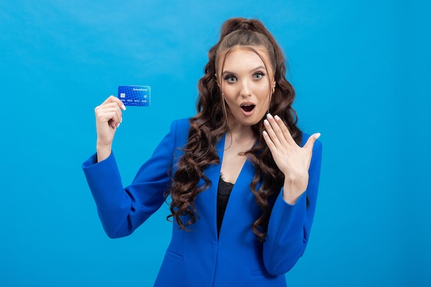 Retrato de uma garota chocada em uma jaqueta com um cartão de débito plástico na mão e a boca aberta