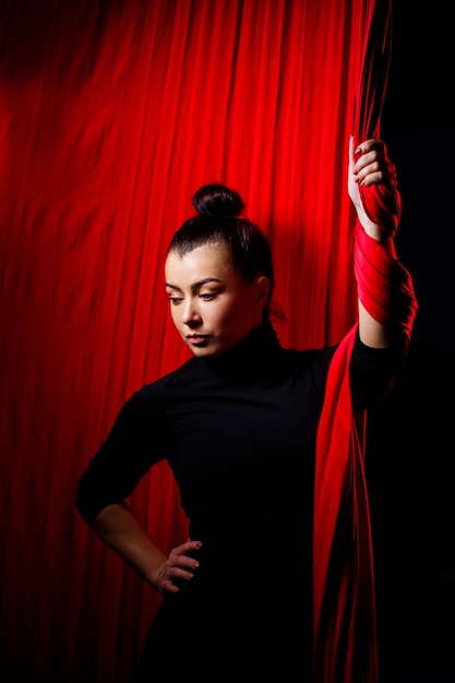 Retrato de uma garota de esportes em um fundo de panos vermelhos para ginástica aérea. Filmagem de estúdio em um fundo escuro,