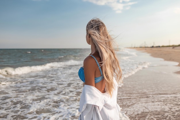 Retrato de uma garota de maiô azul e camisa branca contra o fundo do mar azul e céu claro