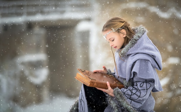 Retrato de uma garota elfa de conto de fadas com um livro de magia nas mãos no cenário de inverno