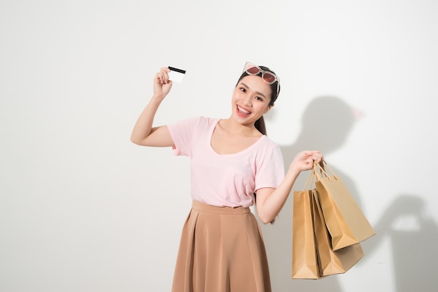 Retrato de uma garota feliz e surpresa segurando sacolas de compras e mostrando o cartão de crédito