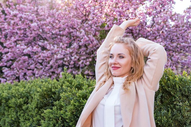 Retrato de uma garota gentil em um parque em flor Uma jovem e bonita mulher com cabelos de cenoura de pé em um parque de sakura em flor levantou as mãos