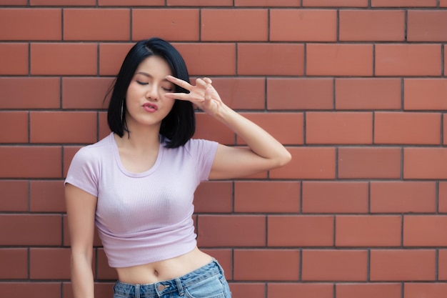 Retrato de uma garota hipster no fundo da parede de tijolos Linda mulher asiática posar para tirar uma foto