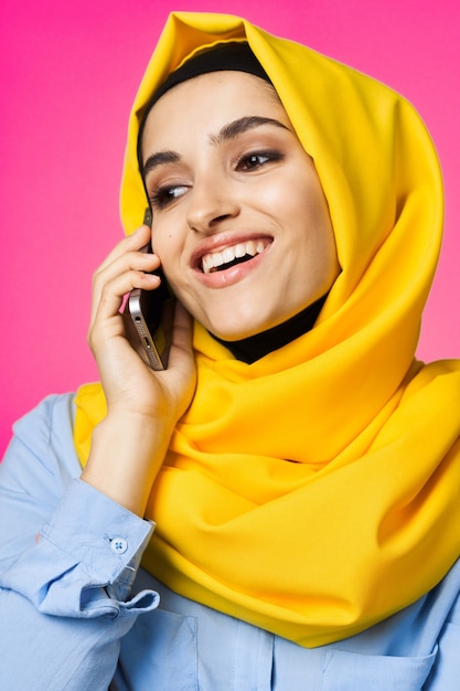 Retrato de uma garota muçulmana em um hijab brilhante com um telefone na mão em um fundo rosa