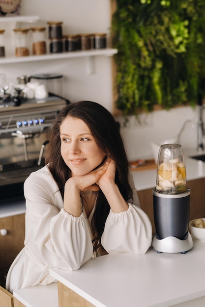 Retrato de uma garota que faz um delicioso coquetel de frutas na cozinha dieta para perda de peso