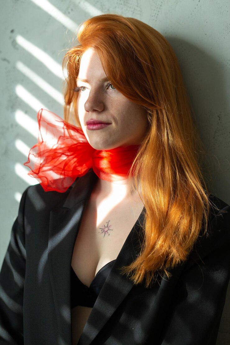 Foto retrato de uma garota ruiva com um lenço vermelho ao redor do pescoço em um terno e luz da manhã suave superior das persianas