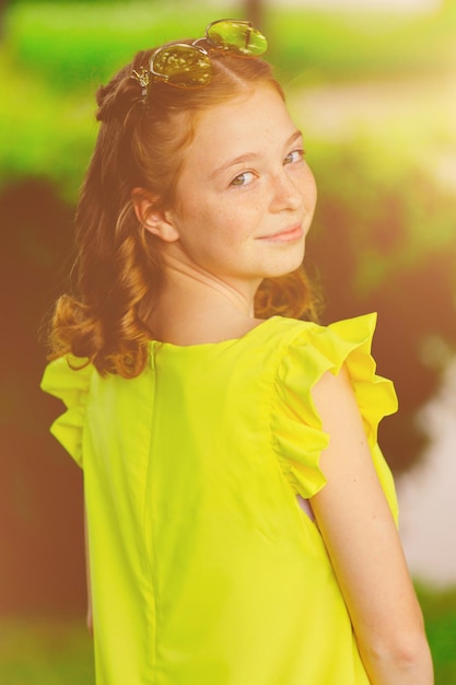Retrato de uma garota ruiva em um vestido amarelo na natureza no verão ao pôr do sol