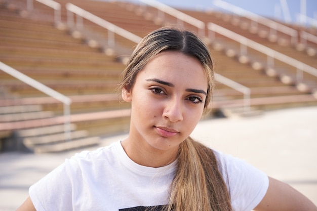 Retrato de uma garota séria olhando para a câmera com plano de fundo de degraus de estádio