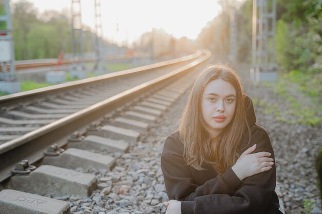 Retrato de uma garota solitária sentada nos trilhos de ferro