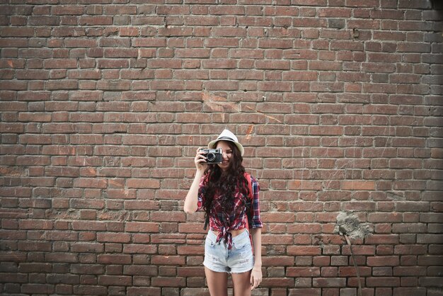 Retrato de uma garota turista com um chapéu tirando fotos na parede do fundo do prédio de tijolos vermelhos