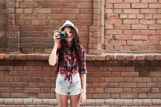 Retrato de uma garota turista com um chapéu tirando fotos na parede do fundo do prédio de tijolos vermelhos