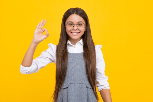 Retrato de uma garotinha adolescente mostrando gesto bem isolado sobre fundo amarelo Conceito de sinal ok Garota feliz enfrenta emoções positivas e sorridentes