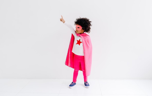 Retrato de uma garotinha afro-americana que joga super-herói no fundo da parede branca Conceito de poder feminino Happy Time