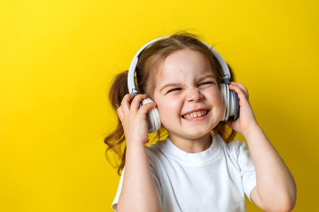 Retrato de uma garotinha alegre ouvindo música com fones de ouvido brancos audiobooks lições de áudio