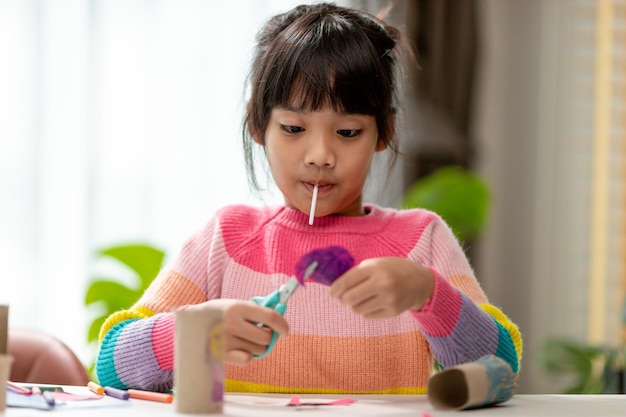 Retrato de uma garotinha asiática cortando um papel em atividades na aula de bricolage na escola Tesoura corta papel
