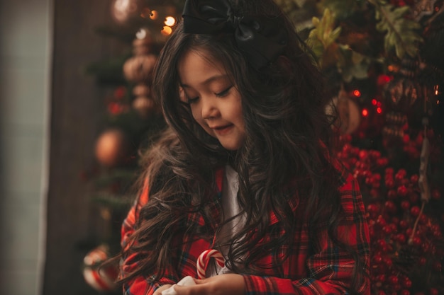 Retrato de uma garotinha asiática sorridente segurando uma caneca vermelha de Natal com marshmallows e bastão de doces