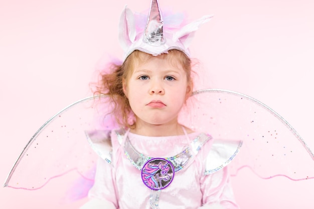 Retrato de uma garotinha fantasiada de unicórnio glitter em fundo rosa.