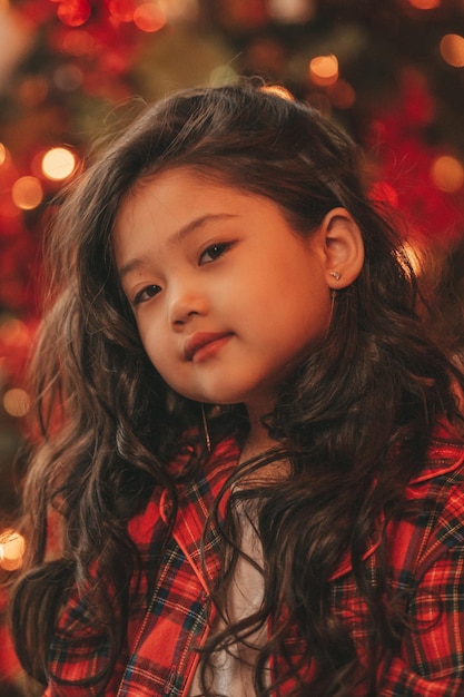 Retrato de uma garotinha sincera e autêntica, sonhadora asiática, de pijama xadrez vermelho, esperando o Papai Noel no Natal