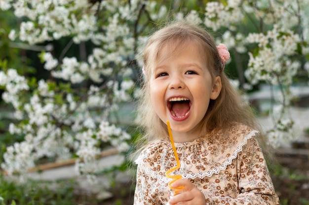 Retrato de uma garotinha sorridente engraçada em um vestido estiloso no jardim florido de fundo