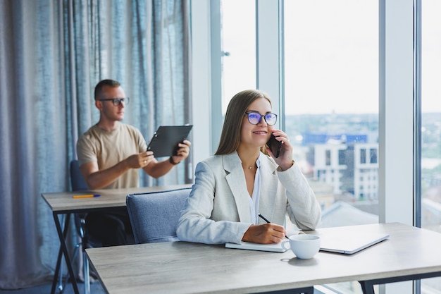 Retrato de uma gerente feminina em trajes formais fazendo trabalho de escritório e falando ao telefone uma chefe feminina europeia bem sucedida em óculos ópticos para correção de visão posando em sua mesa