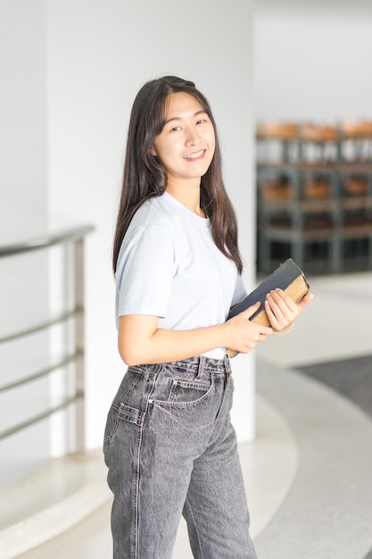 Retrato de uma jovem adolescente asiática alegre estudante universitária em um ambiente descontraído de volta às aulas com estantes de livros no prédio do campus