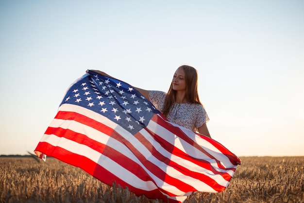 Retrato de uma jovem adolescente com bandeira dos EUA em campo de grãos maduros Bandeira acenando no vento natureza brilhante menina alegre