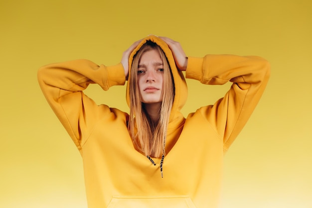 Retrato de uma jovem adolescente triste segurando as mãos na cabeça usando um capuz amarelo casual em tom com fundo