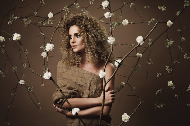 Retrato de uma jovem adorável com penteado afro e bela maquiagem com muitas flores brancas na parede