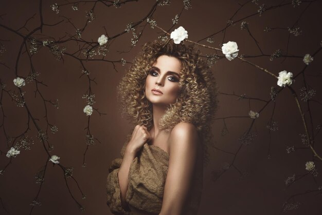 Retrato de uma jovem adorável com penteado afro e bela maquiagem com muitas flores brancas no fundo