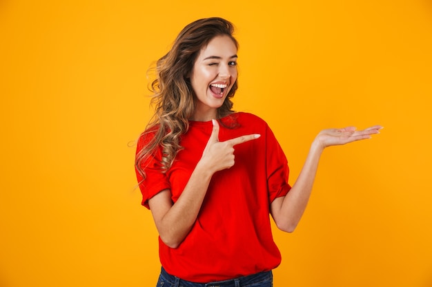 Foto retrato de uma jovem adorável e alegre em pé isolado na parede amarela, apresentando o espaço da cópia